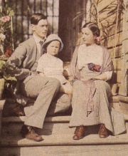 Assis sur les genoux de son père avec sa mère à droite devant le porche de la maison de campagne en 1914.